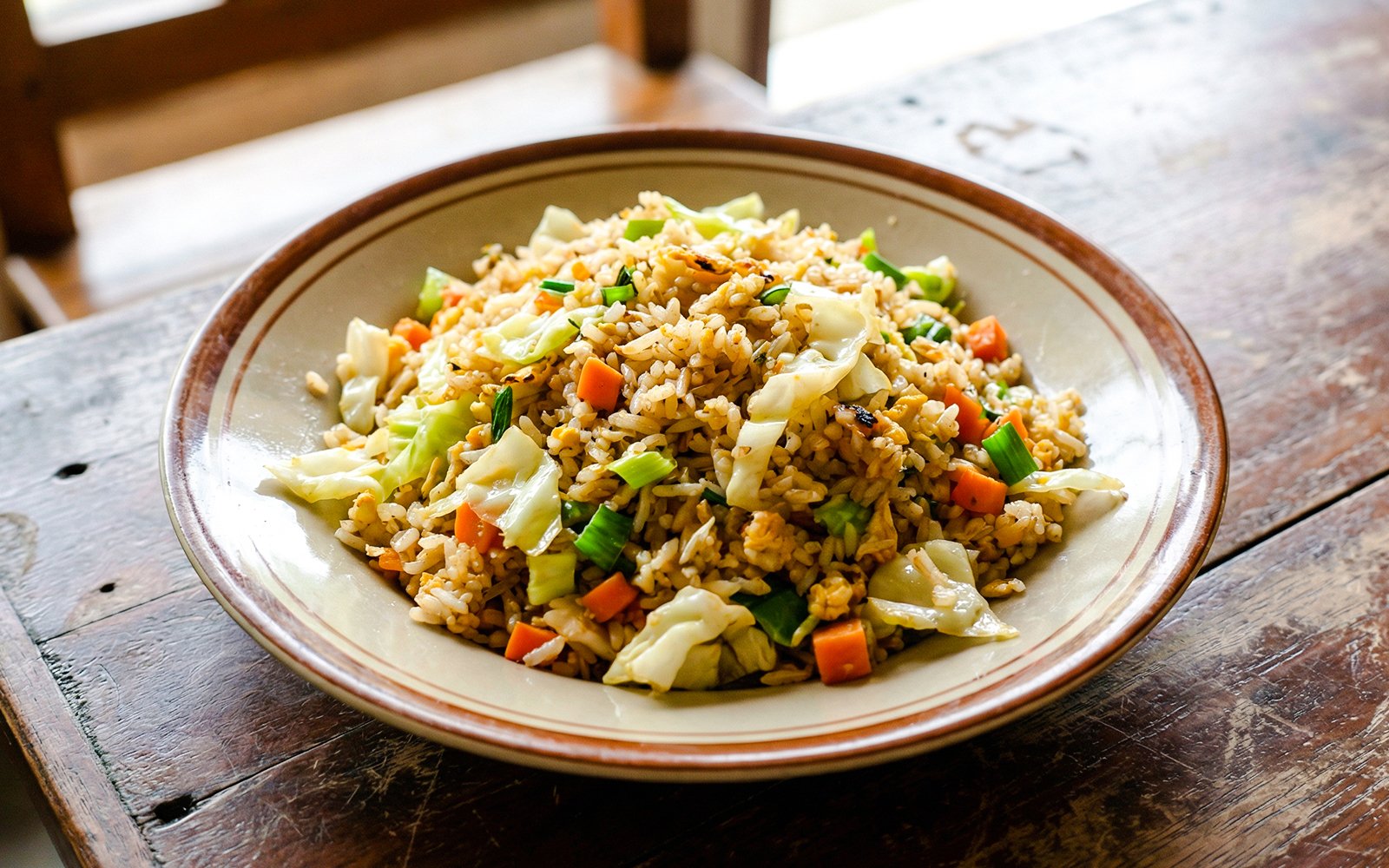 Indonesian fried rice with vegetables on a rustic wooden table.