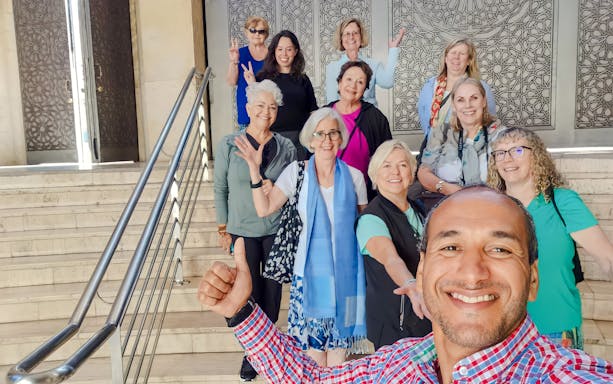 Group of tourists smiling on steps inside Hassan II Mosque, Casablanca, Morocco.