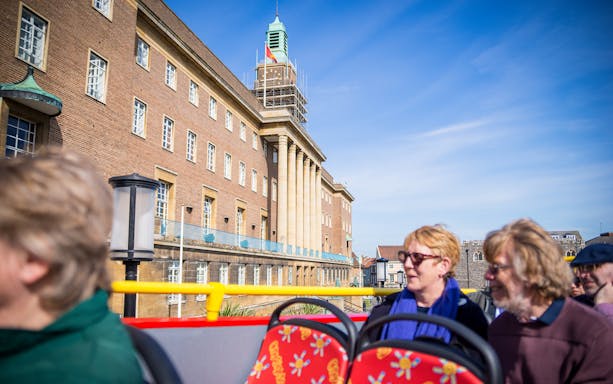 Open-top bus tour passing Norwich City Hall on a sunny day.