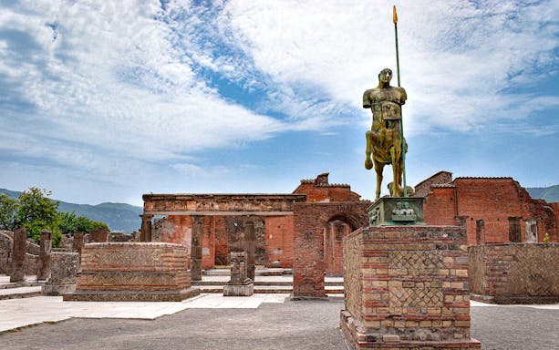 Statue of centaur in Pompeii ruins with ancient brick structures, viewed on a tour from Naples.