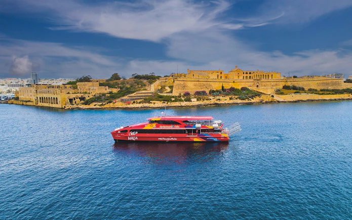 Red tour boat cruising near historic buildings in Valletta, Malta.