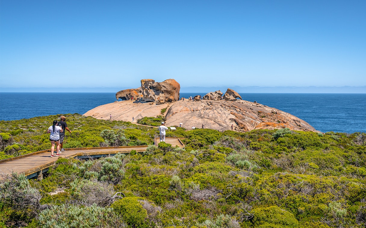 Remarkable Rocks on Kangaroo Island with tourists walking on a boardwalk, ocean in the background.