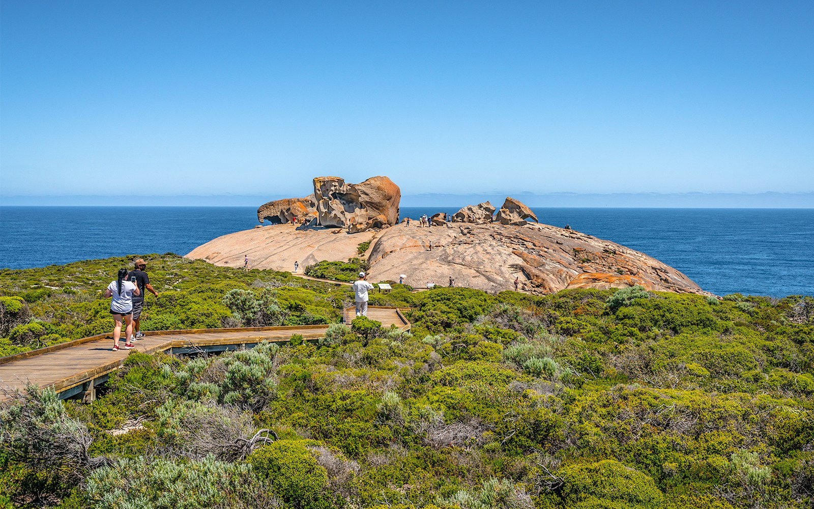 Remarkable Rocks on Kangaroo Island with tourists walking on a boardwalk, ocean in the background.