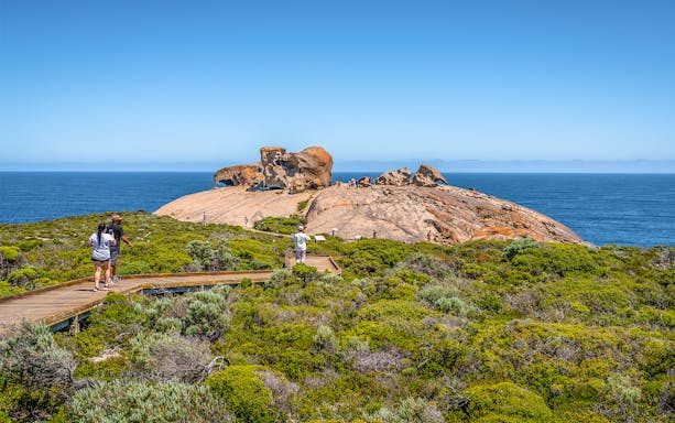 Remarkable Rocks on Kangaroo Island with tourists walking on a boardwalk, ocean in the background.