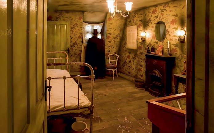 Victorian-style room in Jack the Ripper Museum with bed, fireplace, and figure by window.