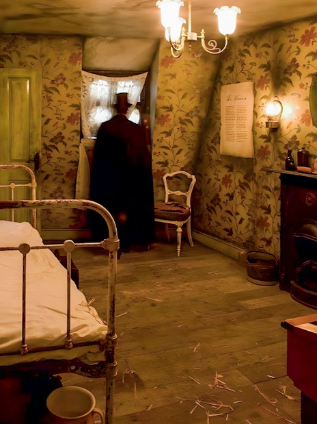 Victorian-style room in Jack the Ripper Museum with bed, fireplace, and figure by window.