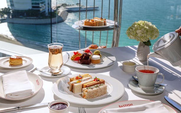 Afternoon tea setup with sandwiches and pastries at Burj Al Arab overlooking the sea.