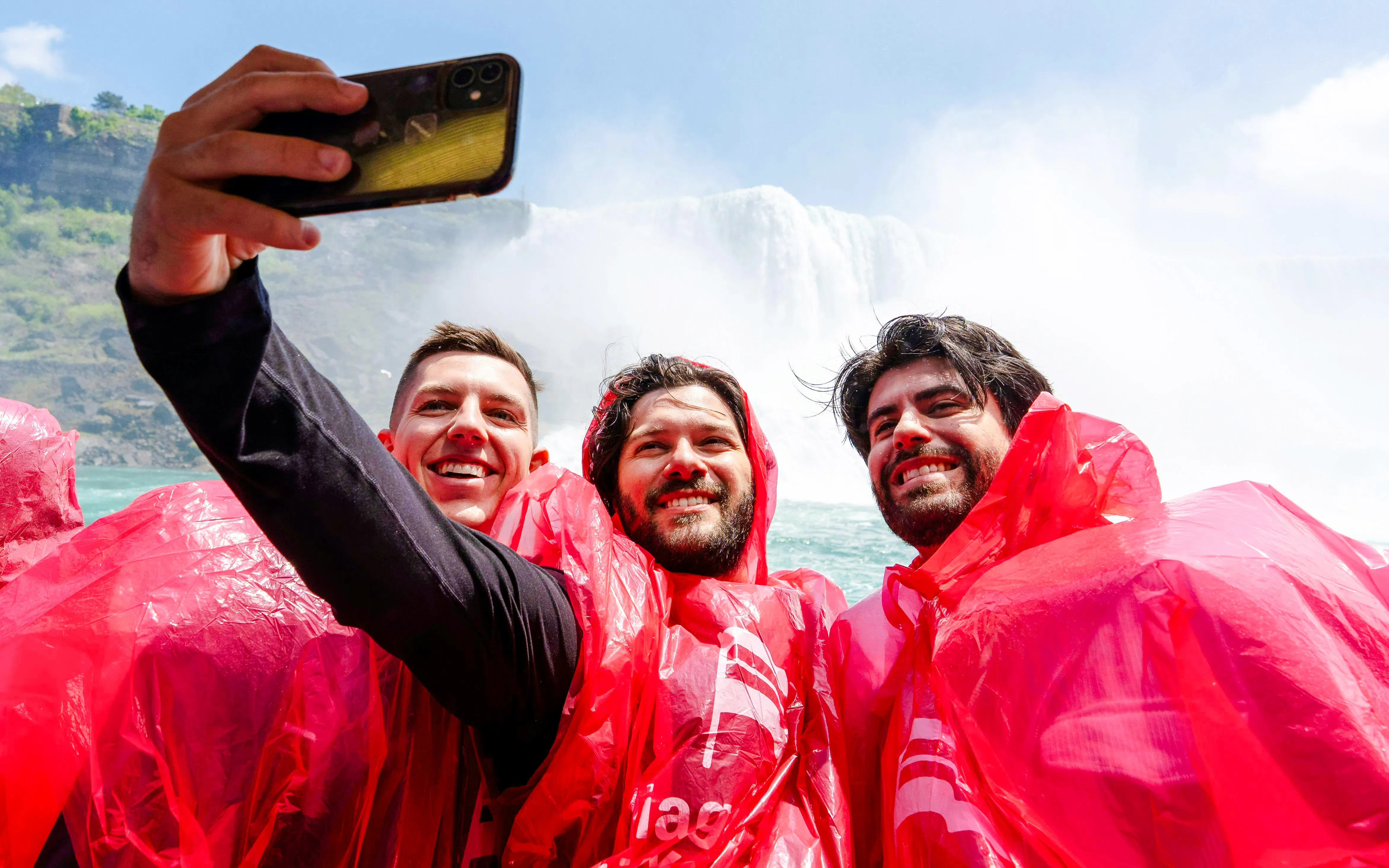 Tourists in red ponchos taking a selfie on a Niagara Falls boat cruise.