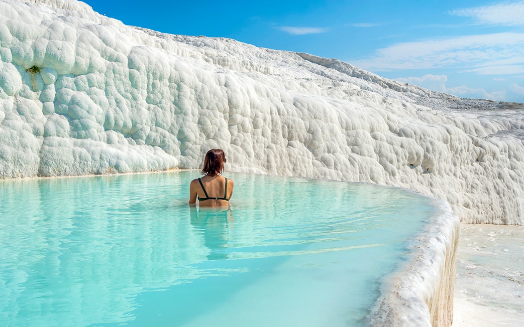 Person bathing in Pamukkale's thermal pool with travertine terraces, Turkey.