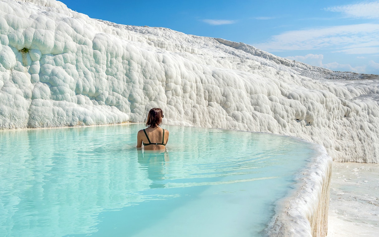 Person bathing in Pamukkale's thermal pool with travertine terraces, Turkey.