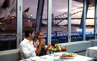 Couple enjoying dinner on a glass boat cruise with Sydney Opera House and Harbour Bridge views.