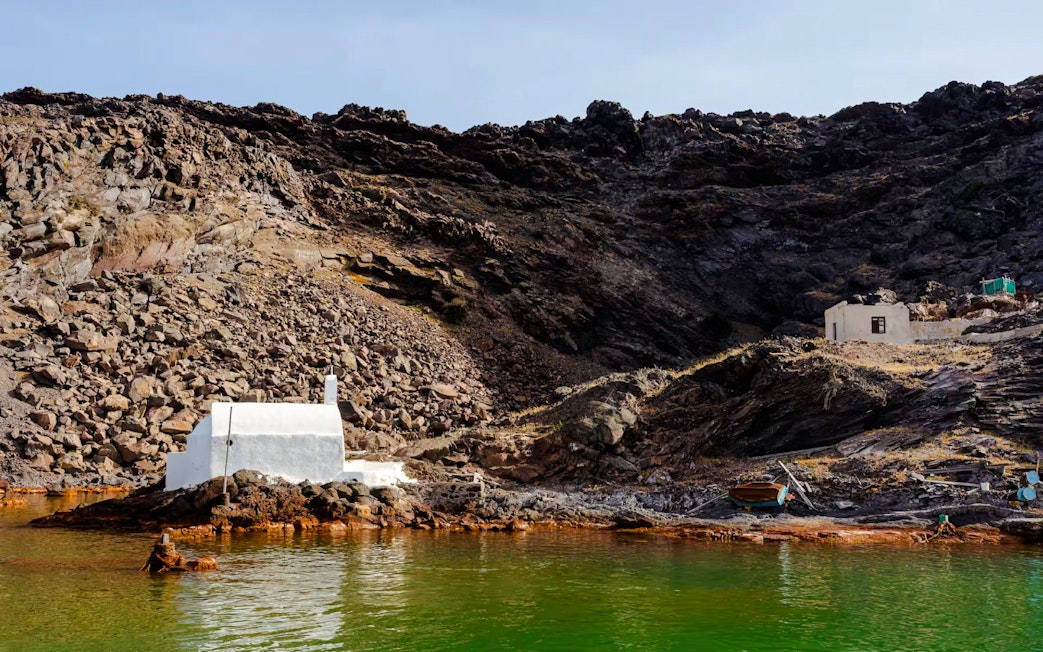 White chapel and rocky landscape at Palea Kameni, Santorini caldera, Greece.