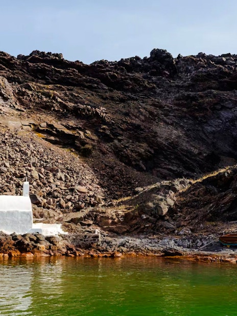 White chapel and rocky landscape at Palea Kameni, Santorini caldera, Greece.