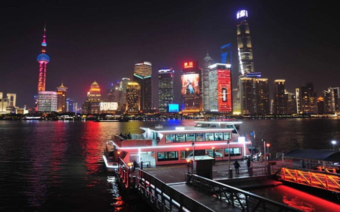 Cruise boat docked at Jinling East Road Pier with Shanghai skyline illuminated at night.