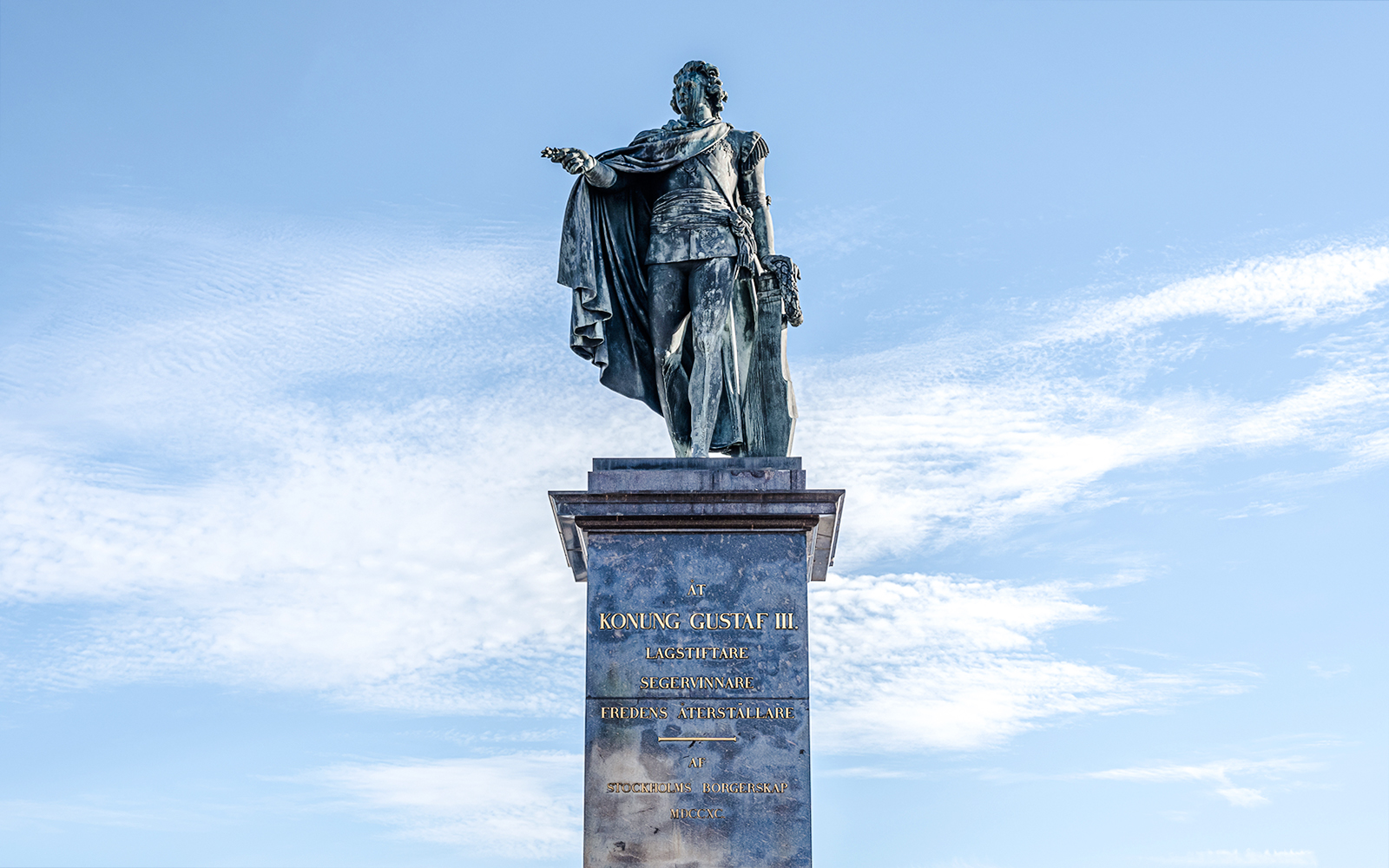 Statue of King Gustav III on a pedestal against a blue sky in Stockholm.