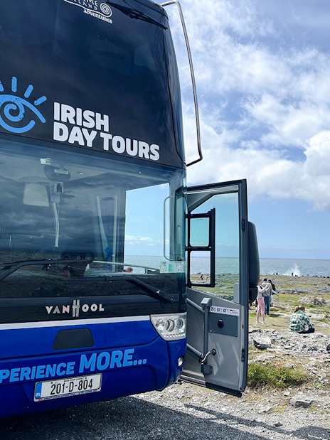 Bus for Irish Day Tours parked near Cliffs of Moher with ocean view.