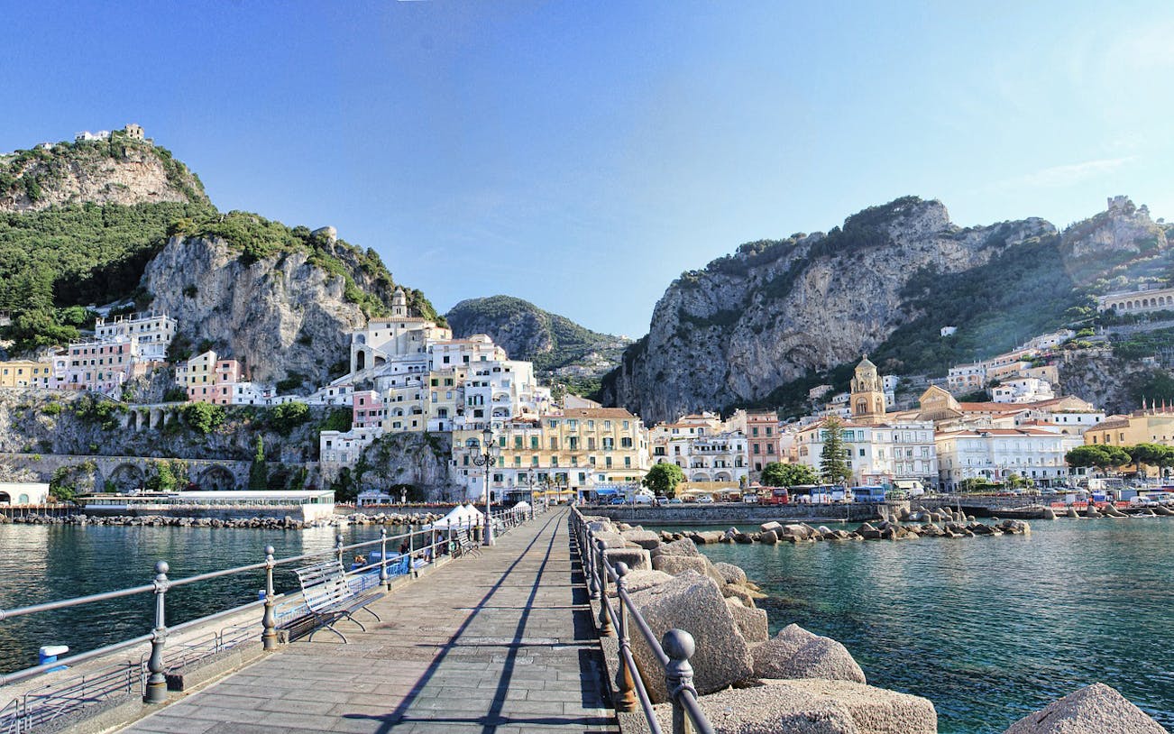 Amalfi Coast view with colorful cliffside buildings and a waterfront promenade.