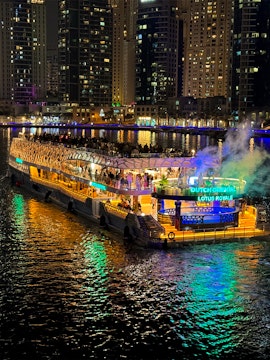 Cruise ship lit up at night on a city waterfront with skyscrapers in the background.