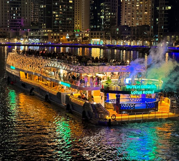 Cruise ship lit up at night on a city waterfront with skyscrapers in the background.
