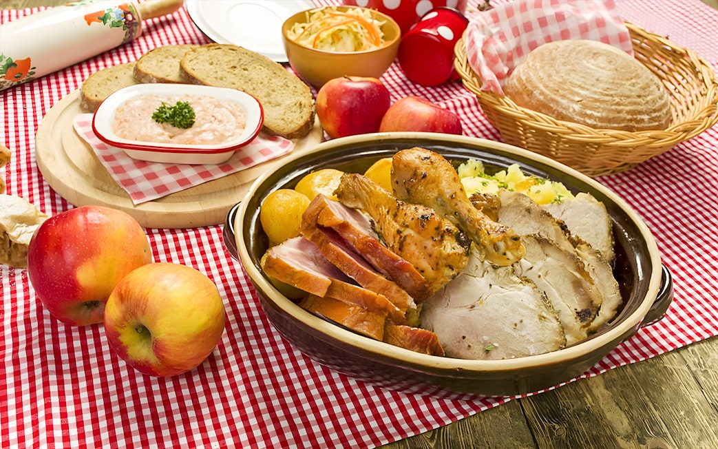 Traditional Czech meal with roast meats, bread, and apples on a checkered tablecloth in Prague.