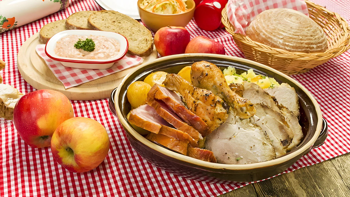 Traditional Czech meal with roast meats, bread, and apples on a checkered tablecloth in Prague.
