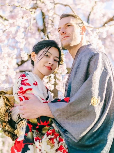 Couple in kimonos posing under cherry blossoms in Japan.