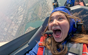 Girl excited during GFORCE Aerobatic Passenger Experience over city landscape.