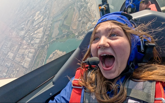 Girl excited during GFORCE Aerobatic Passenger Experience over city landscape.