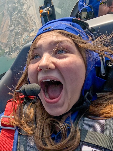 Girl excited during GFORCE Aerobatic Passenger Experience over city landscape.
