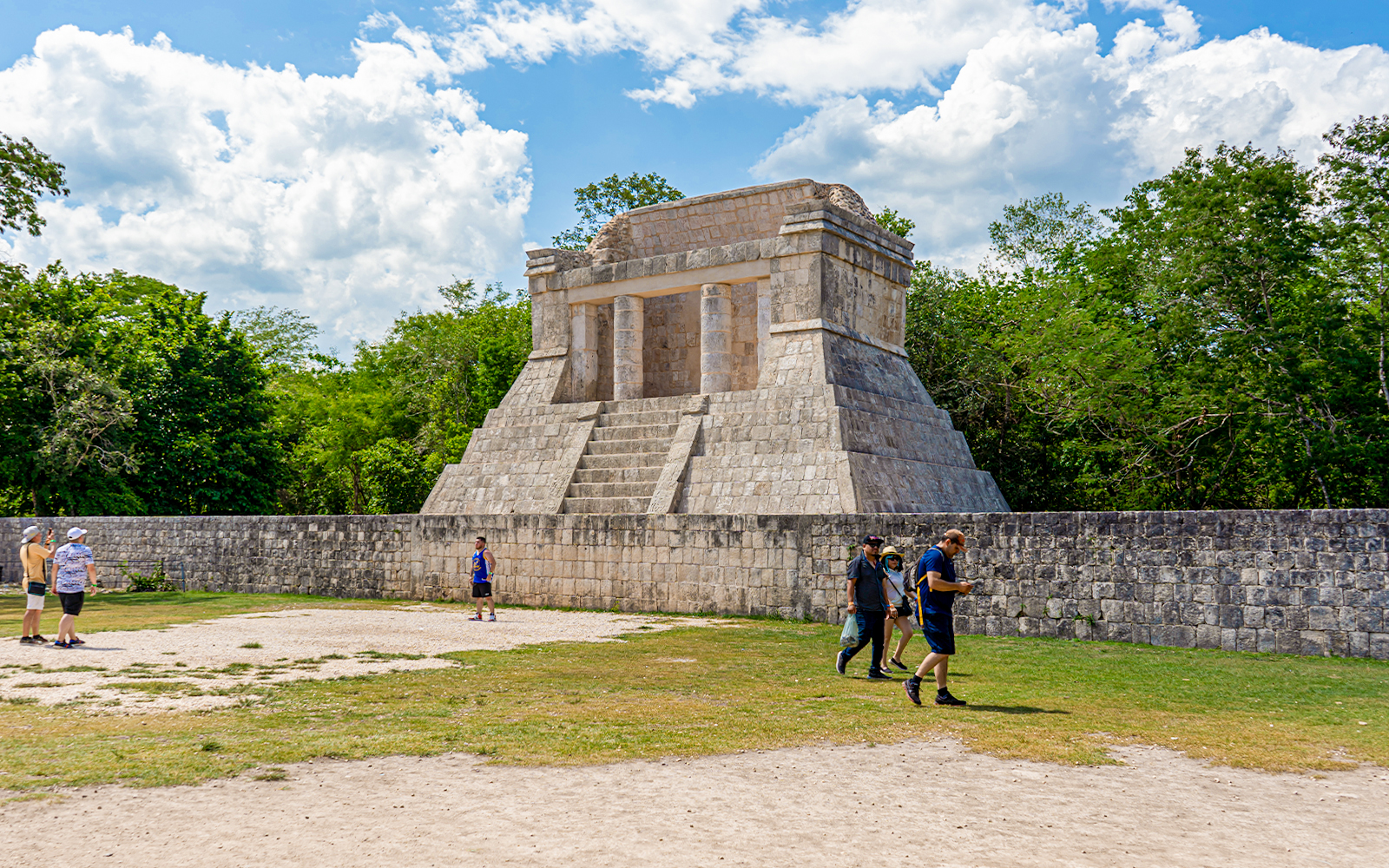 Tourists exploring ancient structure at Chichen Itza during sunrise.