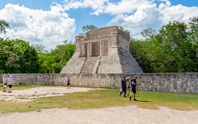 Tourists exploring ancient structure at Chichen Itza during sunrise.