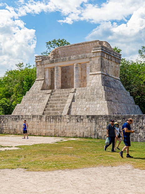 Tourists exploring ancient structure at Chichen Itza during sunrise.