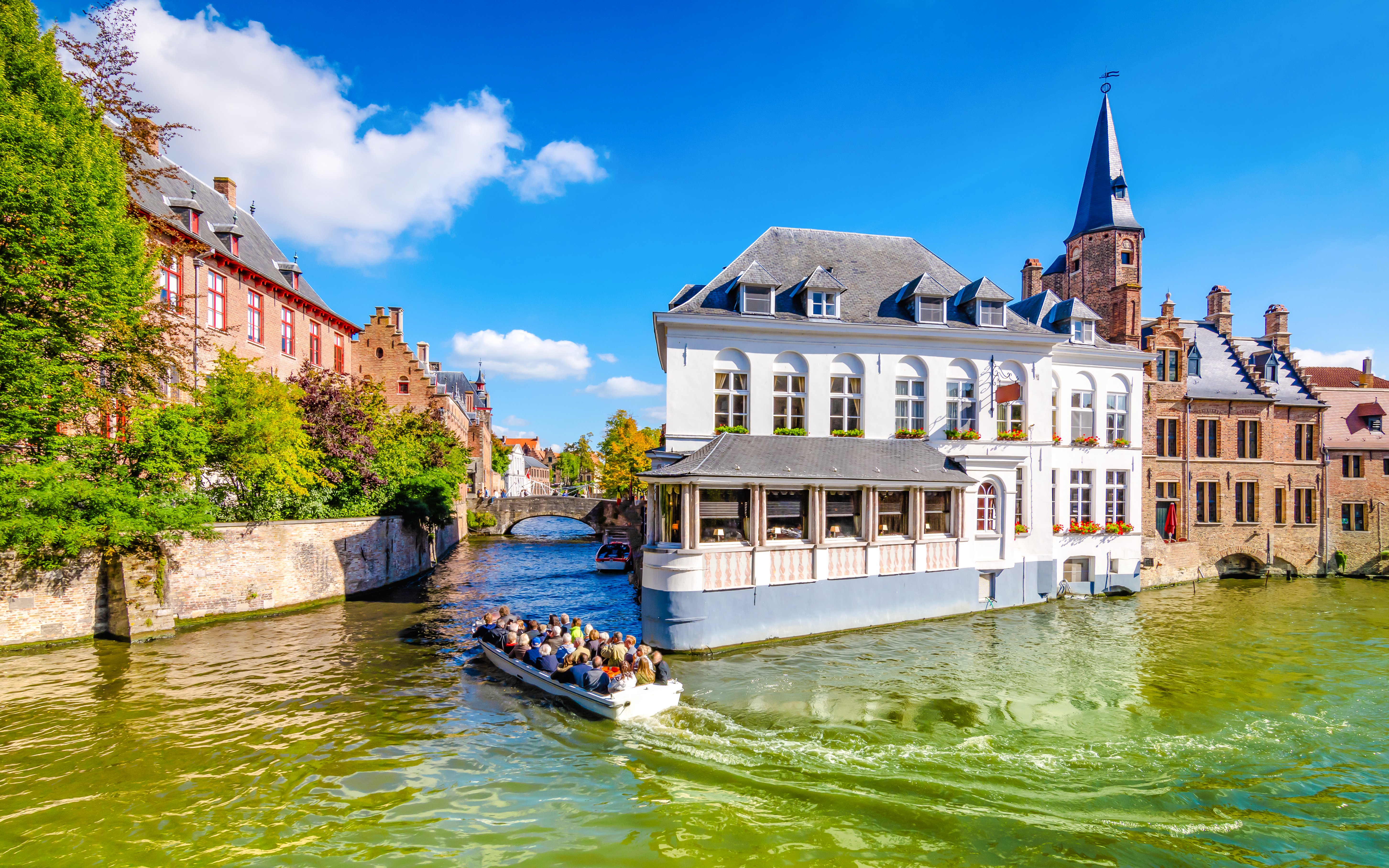Boat tour on a canal in Bruges, Belgium, passing historic buildings and a church spire.