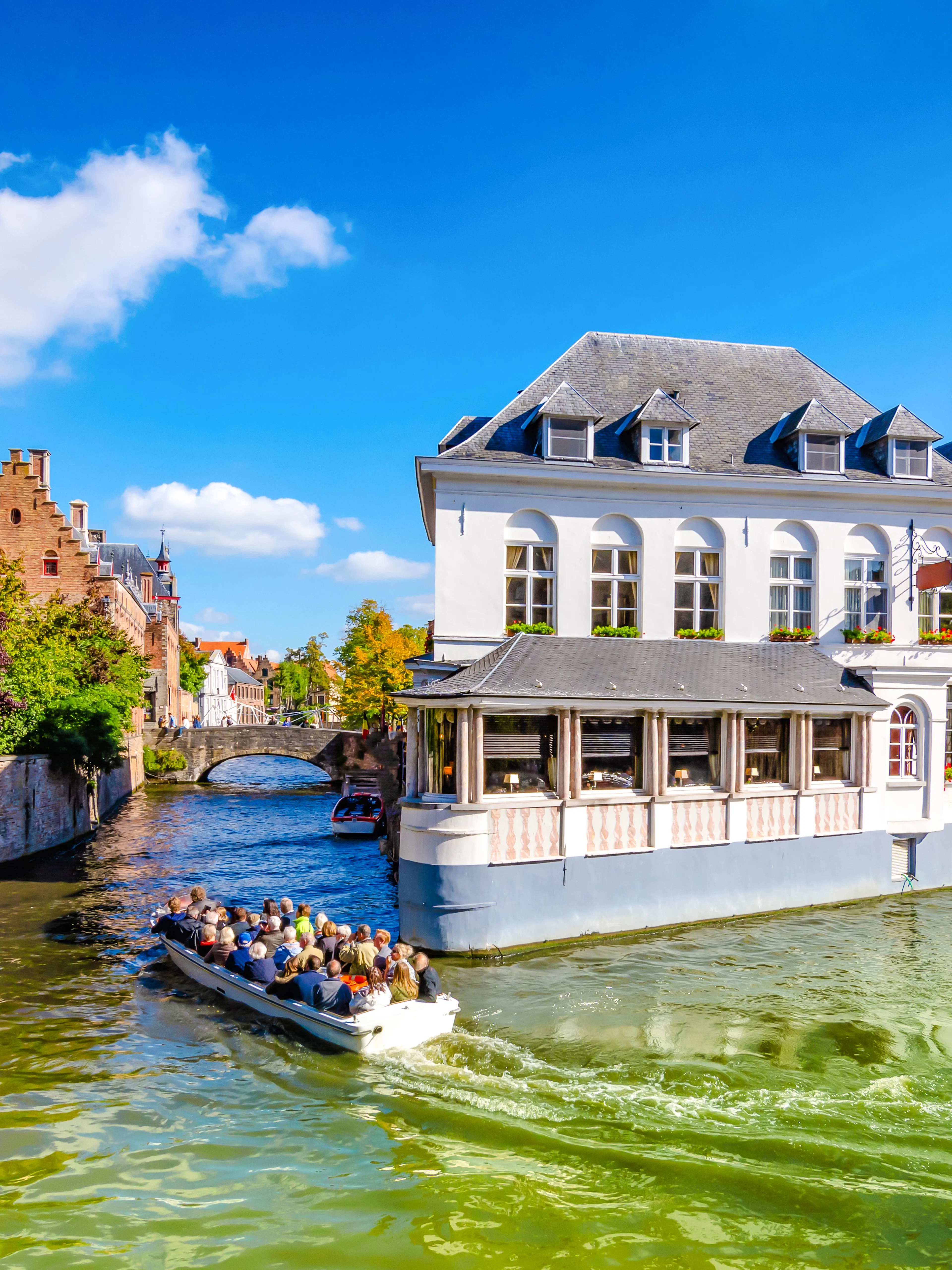 Boat tour on a canal in Bruges, Belgium, passing historic buildings and a church spire.