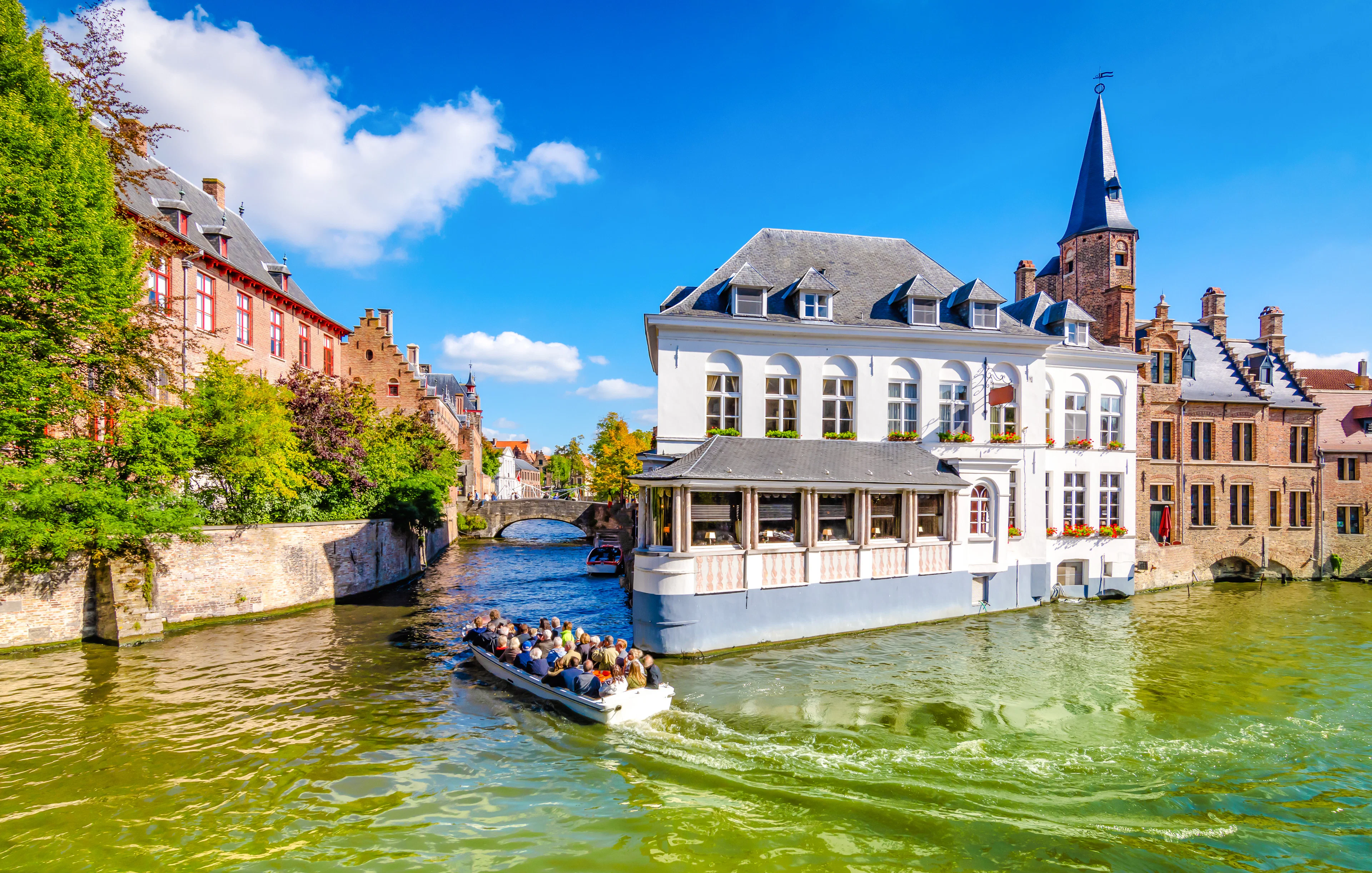 Boat tour on a canal in Bruges, Belgium, passing historic buildings and a church spire.