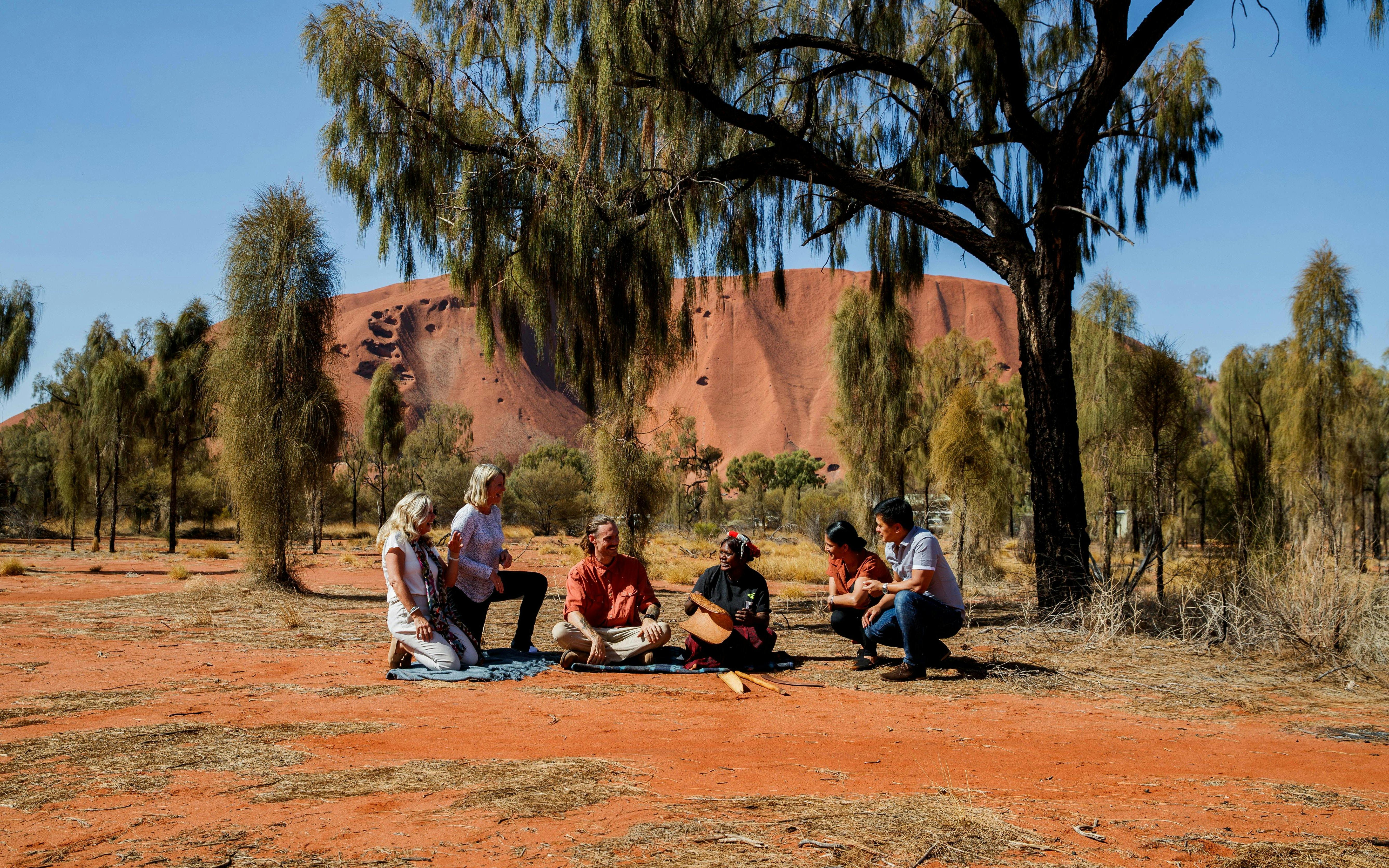 Group listening to Aboriginal stories at Uluru with Kata Tjuta in the background.
