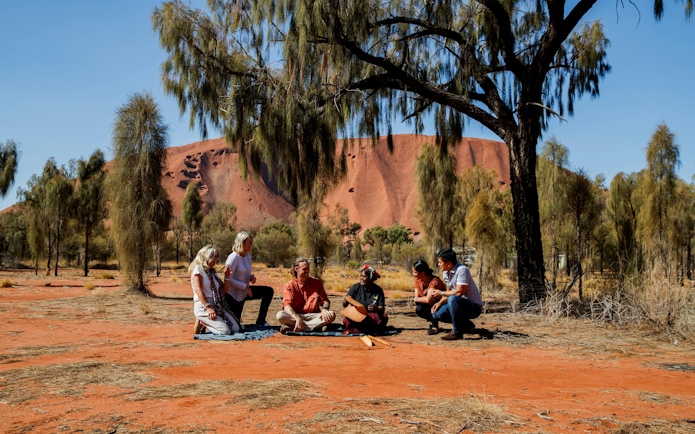 Group listening to Aboriginal stories at Uluru with Kata Tjuta in the background.