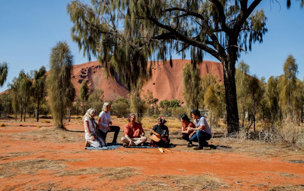 Group listening to Aboriginal stories at Uluru with Kata Tjuta in the background.