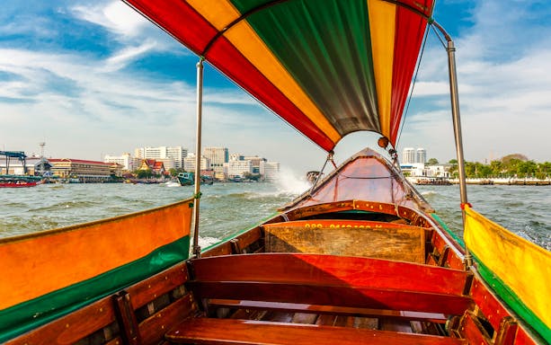 Long tail boat interior on Chao Phraya River, Bangkok skyline in background.