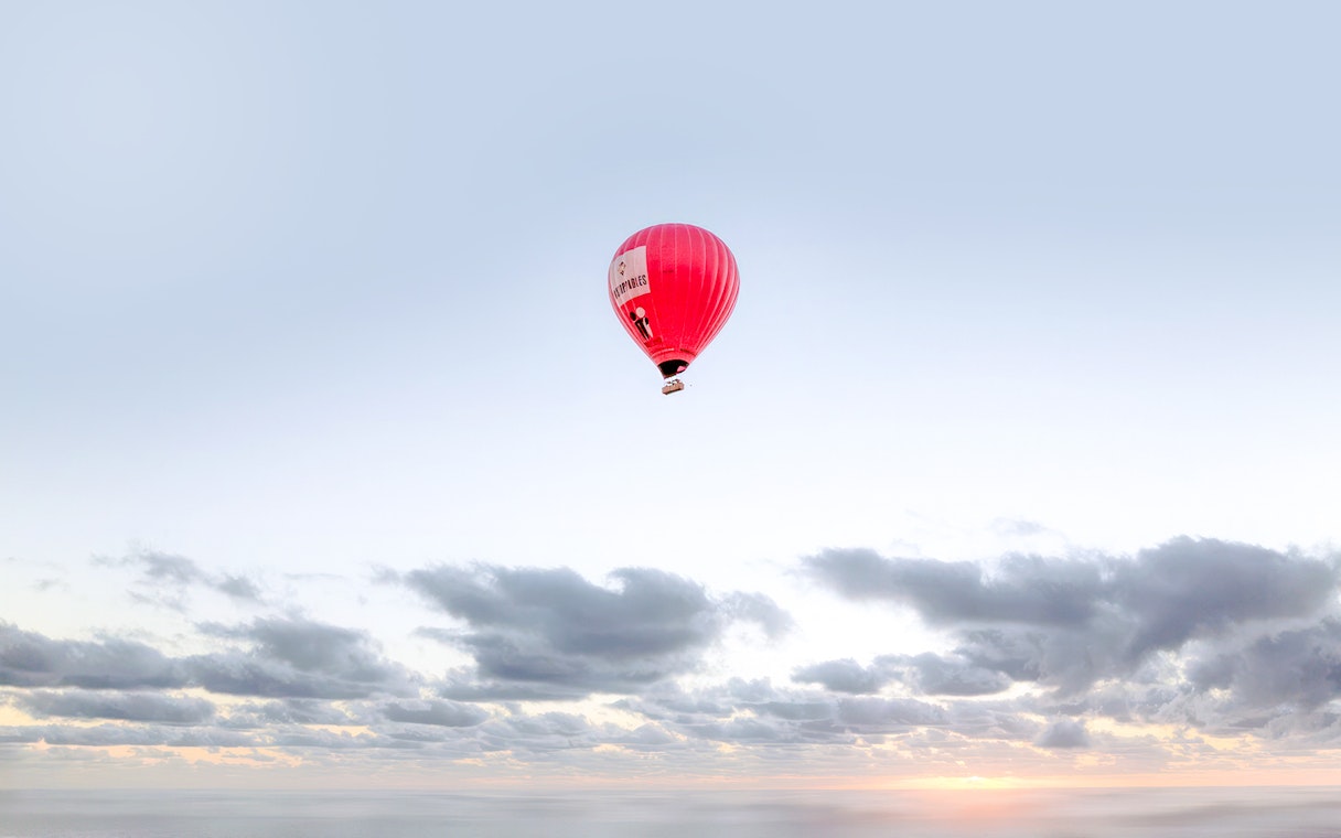 Hot air balloon floating over a cloudy sky at sunrise.