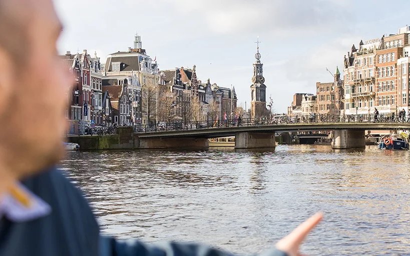 Heineken Canal Cruise with live guide passing Amsterdam's historic Montelbaanstoren tower.