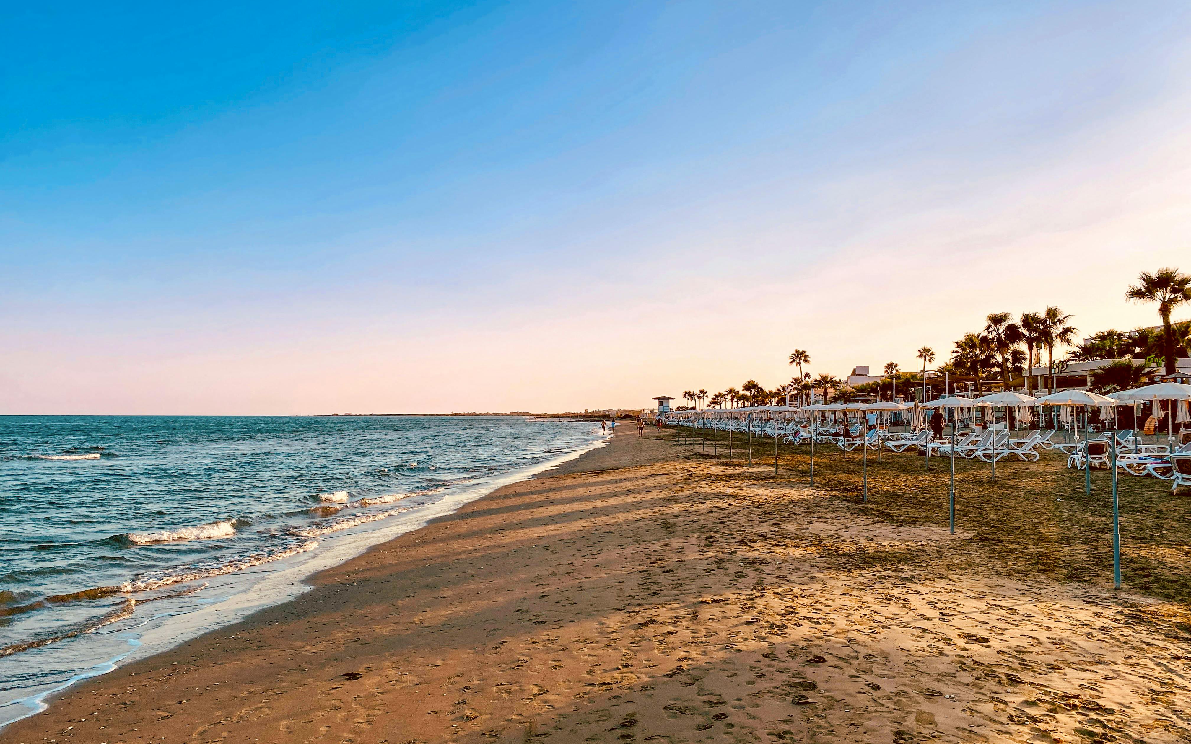 Larnaca Mackenzie Beach with sun loungers and umbrellas at sunset.