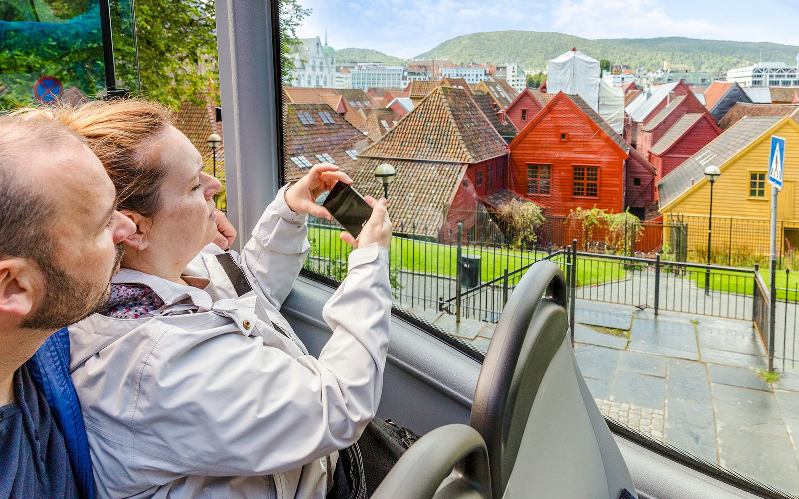 Tourists on Bergen Hop on Hop off bus viewing colorful wooden houses in Bergen, Norway.