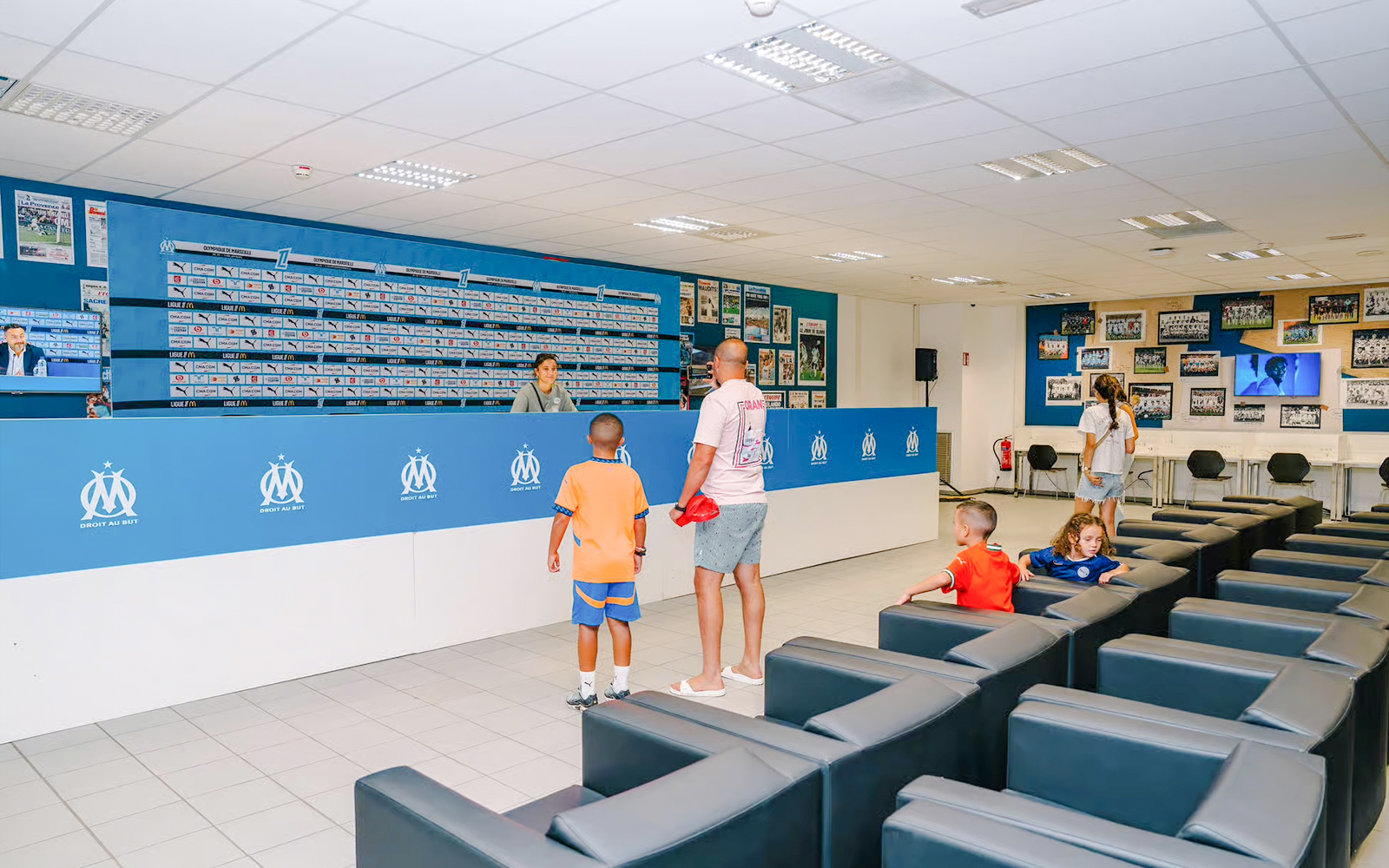 Press room at Velodrome Stadium tour with visitors exploring the space.