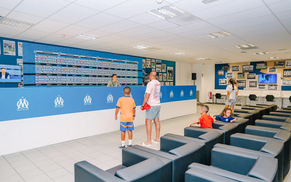 Press room at Velodrome Stadium tour with visitors exploring the space.