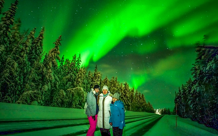 Guests on Northern Lights Chase tour under aurora borealis in snowy landscape.