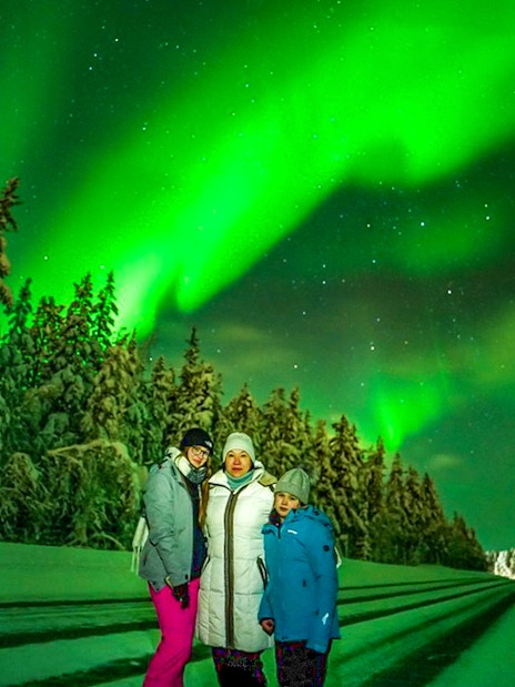 Guests on Northern Lights Chase tour under aurora borealis in snowy landscape.