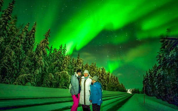 Guests on Northern Lights Chase tour under aurora borealis in snowy landscape.
