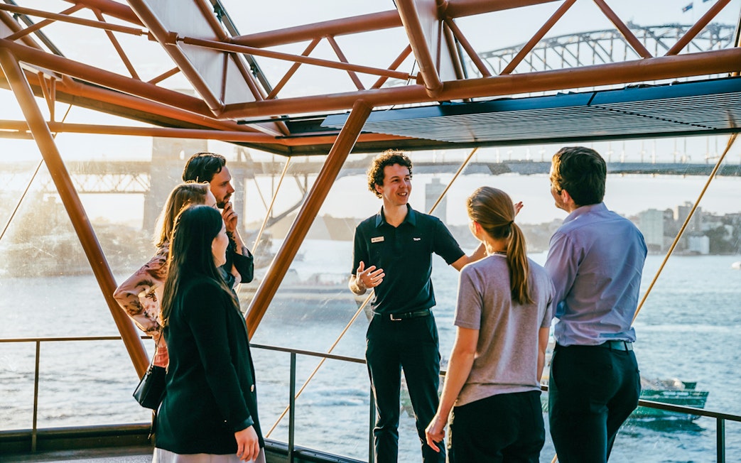 Tour guide leading a group at Sydney Opera House with Harbour Bridge view.