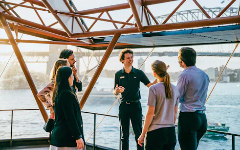 Tour guide leading a group at Sydney Opera House with Harbour Bridge view.